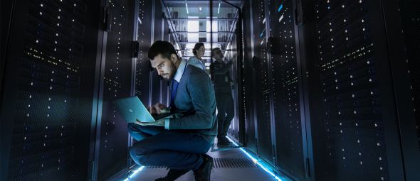 IT Technician Works on Laptop in Big Data Center full of Rack Servers. Multiple People Works at Data Center at the same time.