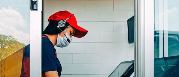 A fast food worker with a mask on working in the drive through window. 