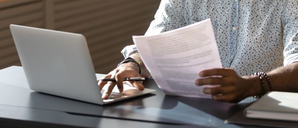African American man holding document while working on computer.