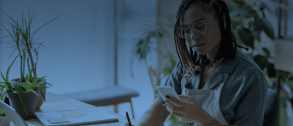 young african american florist in eyeglasses looking at smartphone and writing order in notebook in flower shop